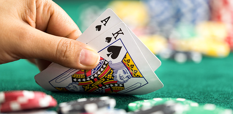Detaljbild på hand som håller två spelkort, spader ess och spader kung. I förgrund och bakgrund ser mar spelmarker.