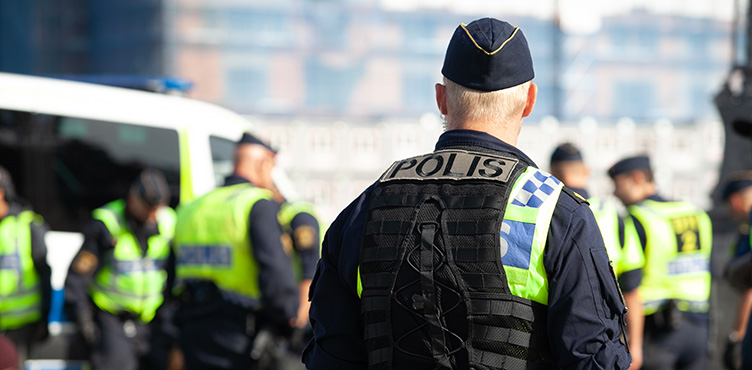 Swedish police officers in neon vests. In the foreground, a policeman is seen from behind, the rest are blurred.