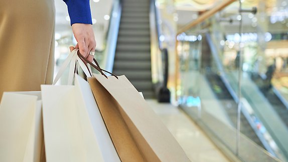 Kvinna som bär shoppingkassar i rulltrappa i köpcenter.